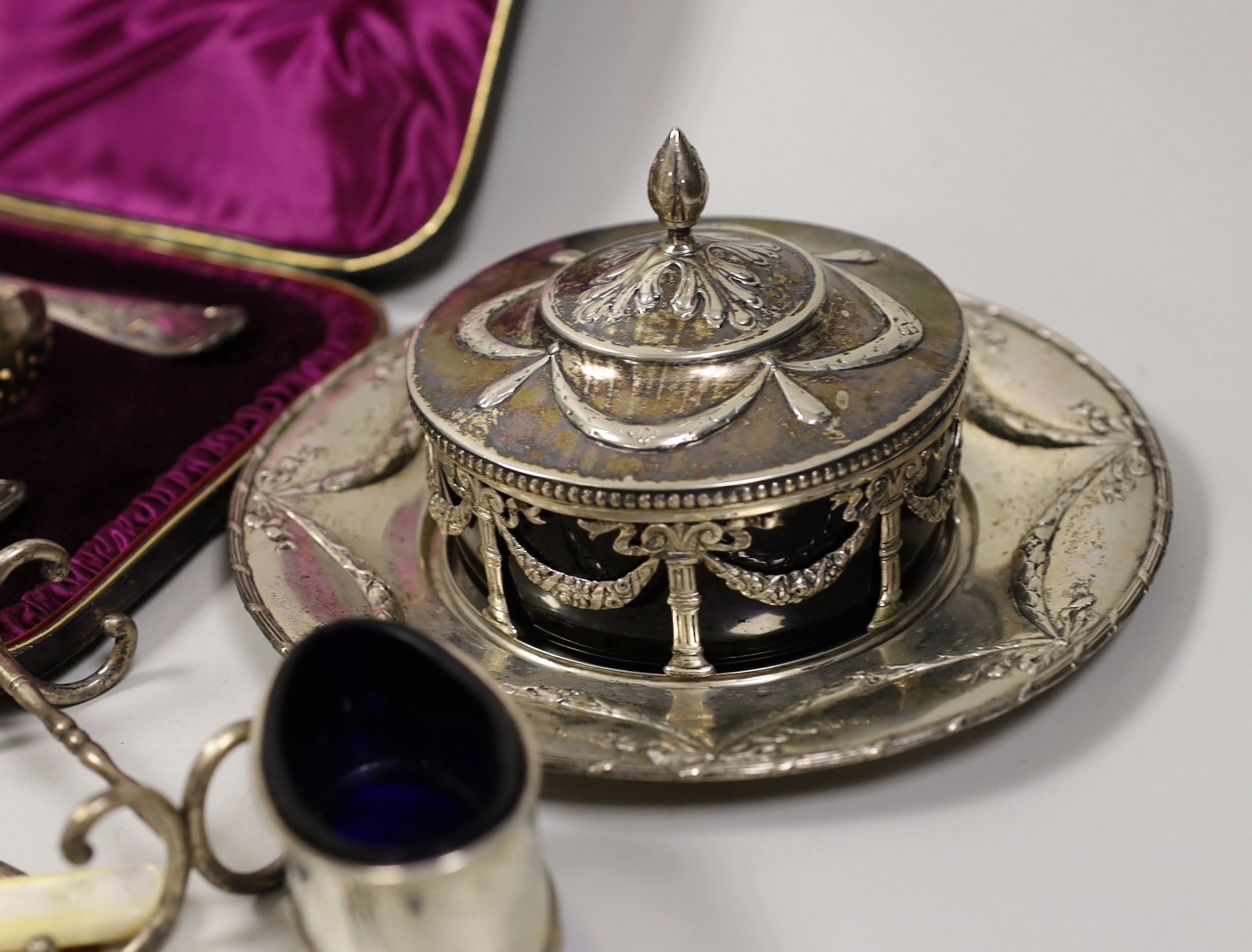 A late 19th century Hanau white metal butter dish stand, with blue glass liner, diameter 18.3cm, a sterling mounted cigarette box, a cased Victorian three piece silver cutlery dessert set, a pair of Victorian silver fidd